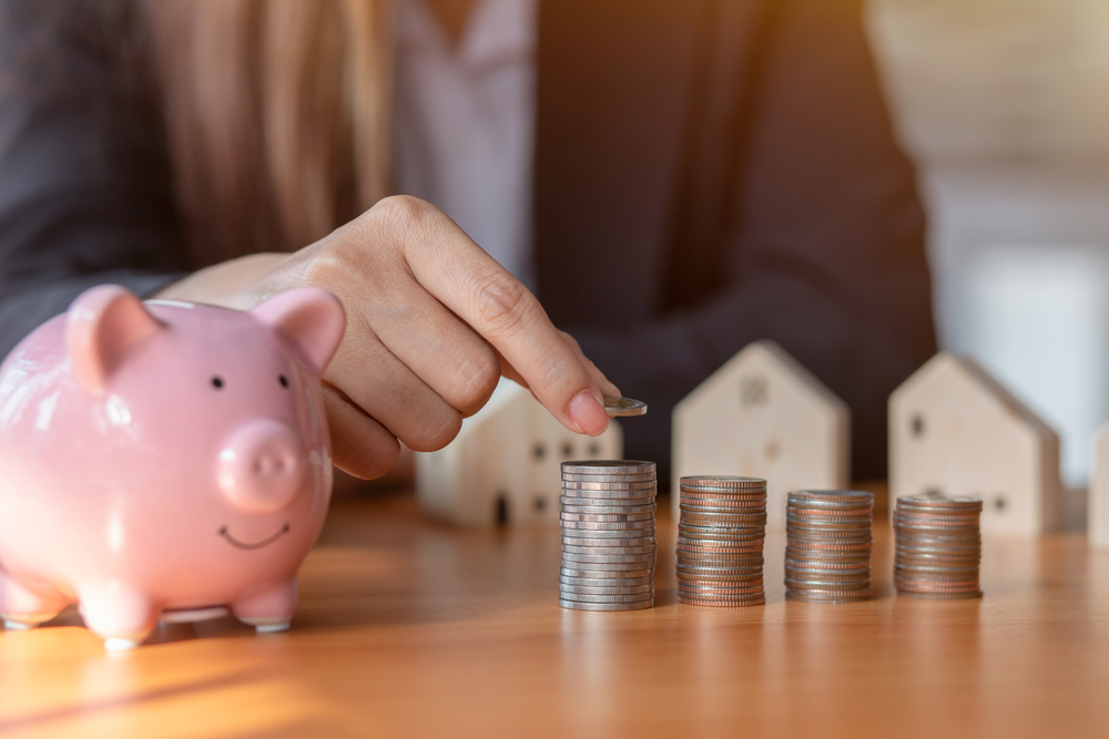 Hand putting money coin stack with wooden house,Property investment and house mortgage financial concept.