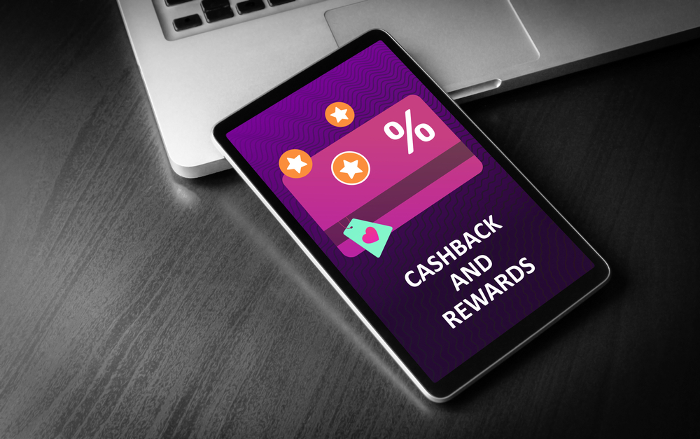 Cashback and Rewards - loyalty program and retail customer money refund service concept. Tablet PC lying on a wooden table with cashback discount card and rewarding marketing points on the screen