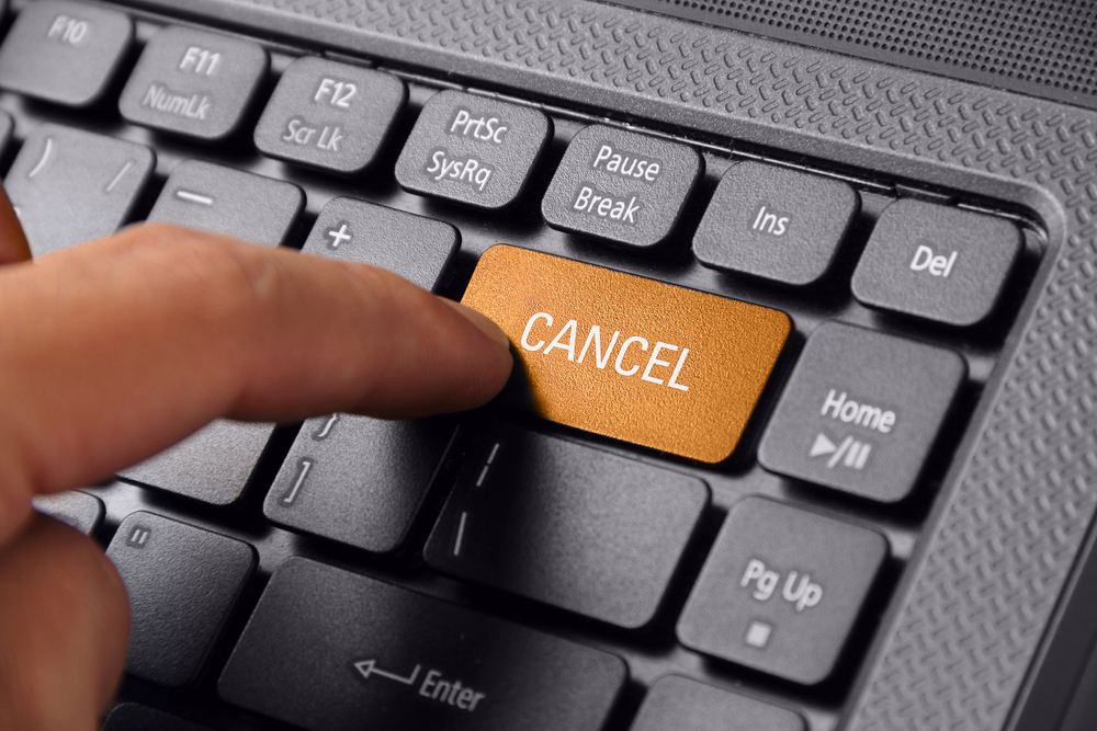 Gesture of a hand finger pushing the CANCEL button on laptop representing cancelling a subscription
