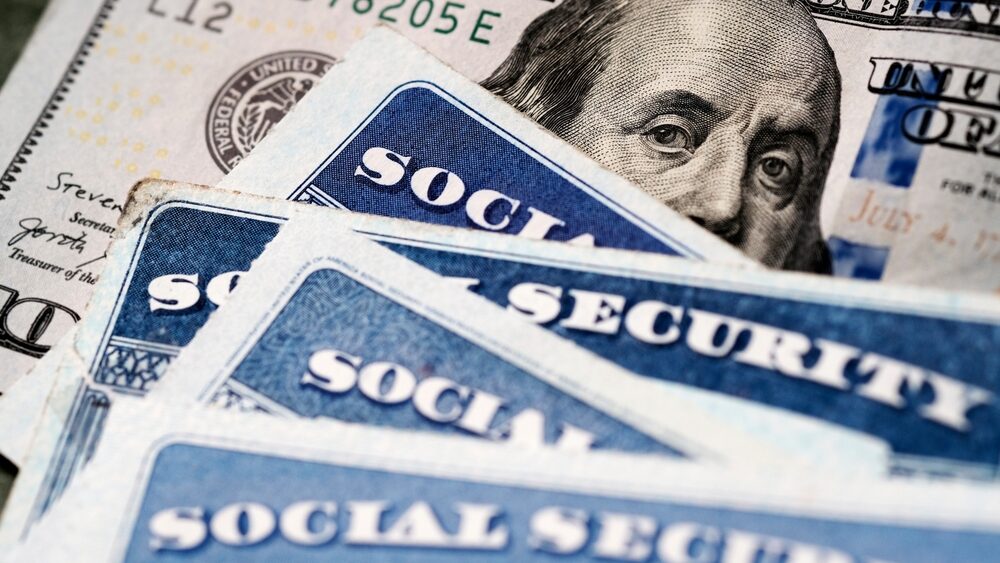 Several Social Security Cards on a US United States one hundred dollar bill $100 system of benefits for retired elderly people representing the new FRA changes from 2025