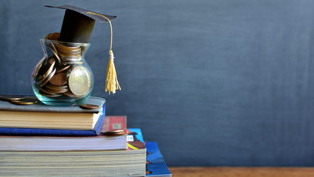 A pot filled with coins and topped with graduate hat placed on the stack of books representing the concept of knowledge is power