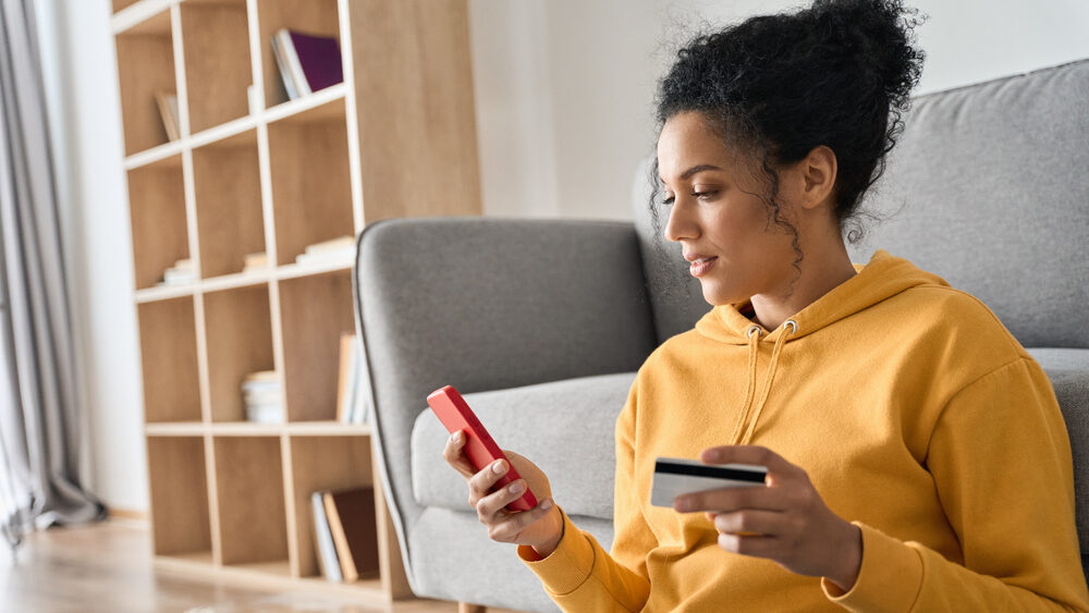 Young women using her credit card online with smartphone and credit card in hands